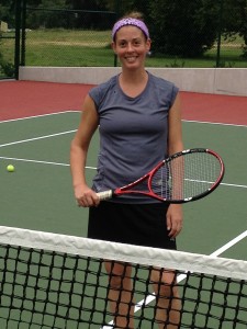 A lady tennis player standing at the net holding a tennis racket.