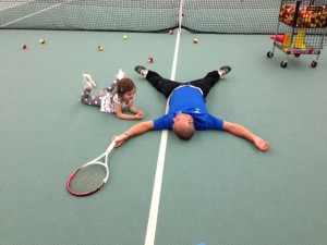 A tired tennis instructor on a tennis court with a young student listening.